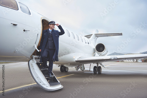 Full length side view outgoing pilot standing on stairs of aircraft. Profession concept