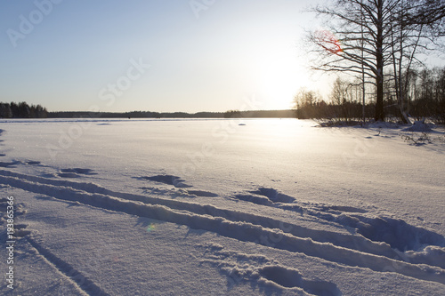 Wintry scenery in Finland. Very cold day in Finland, path and ski tracks in the snow. Sunset behind the lake, some flare added in the image. Deep snow.