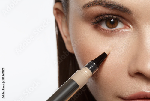 Close up of calm girl applying foundation under eye area by special brush. Macro concept. Isolated and copy space