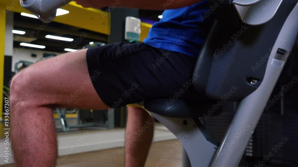 A fit man trains on a machine in a gym - closeup from the side A fit man trains on a machine in a gym - closeup from the side