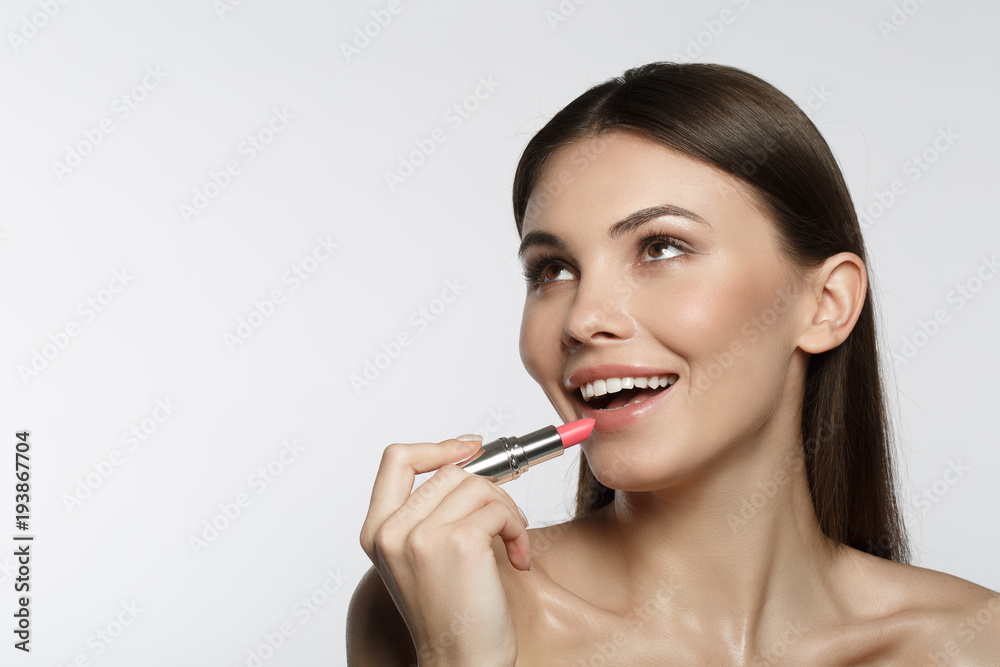 Portrait of cheerful girl applying pink lipstick with delight. She is looking up and smiling. Isolated and copy space Portrait of cheerful girl applying pink lipstick with delight. She is looking up and smiling. Isolated and copy space