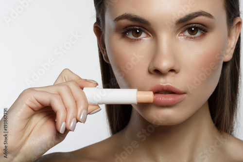 Close up of beautiful female face. Calm girl is holding chapstick near her lips. Isolated