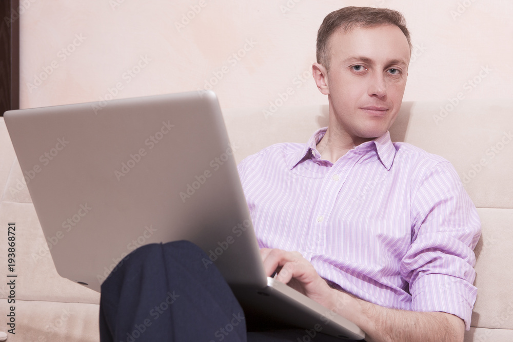 Youth Concepts and Ideas. Handsome Man in Business Style Clothing Sitting on Couch while Legs Folded. Posing with Laptop Computer. Youth Concepts and Ideas. Handsome Man in Business Style Clothing Sitting on Couch while Legs Folded. Posing with Laptop Computer.