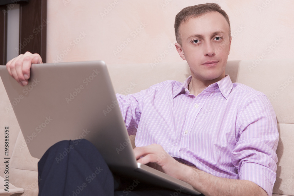 Youth Concepts. Handsome Man in Business Style Clothing Sitting on Couch while Legs Folded. Posing with Laptop Computer. Youth Concepts. Handsome Man in Business Style Clothing Sitting on Couch while Legs Folded. Posing with Laptop Computer.