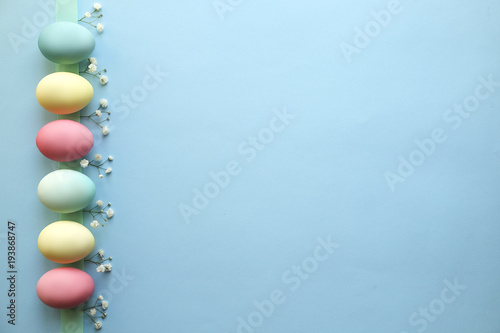 Different pastel color Easter eggs laid and arranged in beautiful composition with white wildflowers. Greeting card with copy text space.