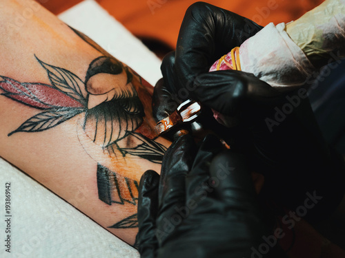 Tattoo artist at work. Woman in black latex glove tattooing a young man's hand with colorful picture in studio. Macro.