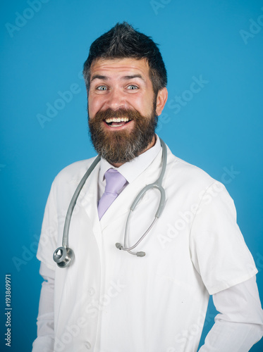 Cheerful smiling male doctor with beard. Bearded doctor in white dress with stethoscope on neck. Health care and medicine - young man doctor with tie isolated on green background.