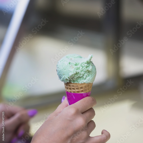 Pistachio ice cream mix in waffle cone, Female hand. Popular delicacies for adults and children.Selective focus. Real scene