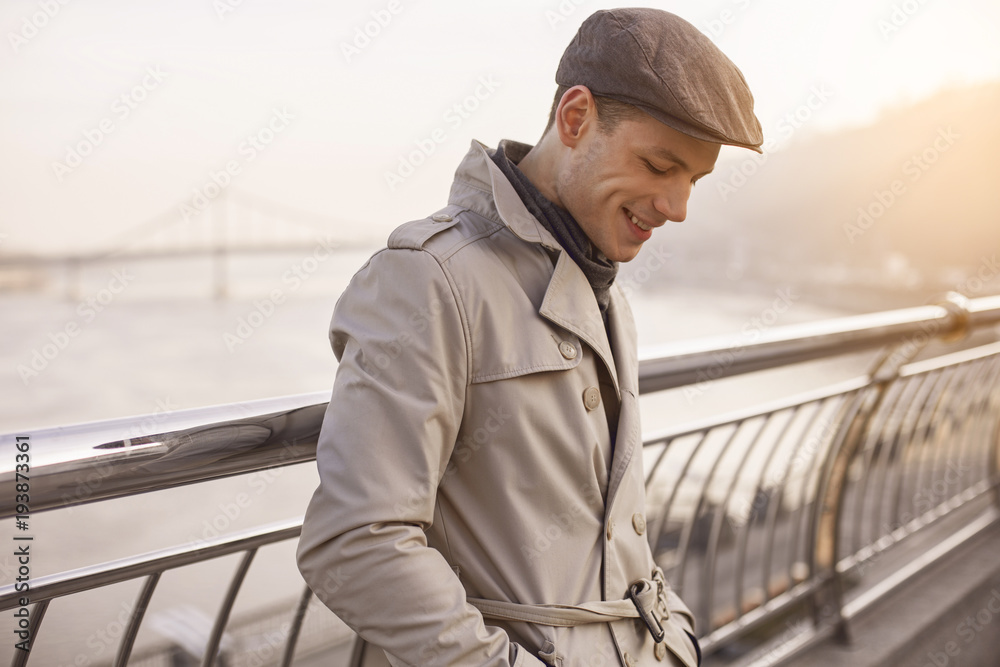 I feel good. Side view profile of cheerful stylish guy is standing on street and looking down with smile. He is holding hands in pockets of his coat I feel good. Side view profile of cheerful stylish guy is standing on street and looking down with smile. He is holding hands in pockets of his coat