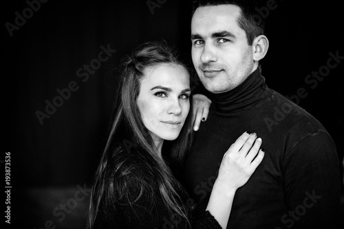 Black and white photo of an amazing couple who stands on a black background and looks at the camera