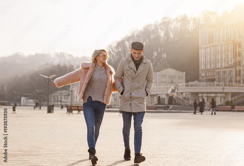 Fototapeta premium Walking together. Full length of happy young couple on date is having fun outdoors. They are going hand in hand while enjoying sunny spring day