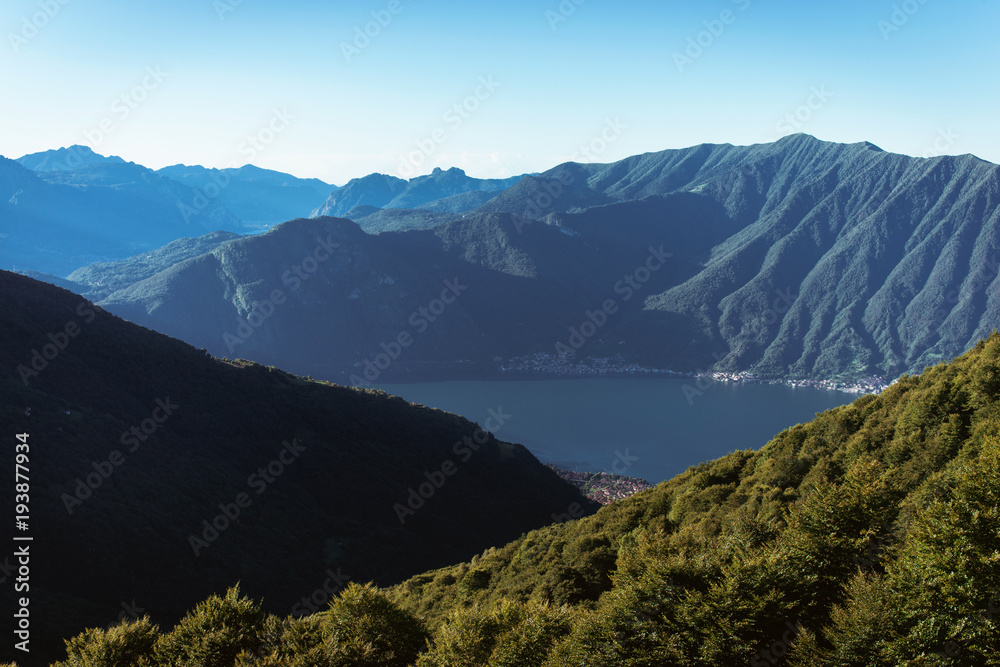 Panoramic View of beautiful landscape in the Italian Alps with fresh green meadows and snow-capped mountain tops in the background on a sunny day with blue sky and clouds in springtime.