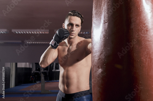 one boxer, punching boxing bag, indoors room. shirtless, wearing boxing gloves.