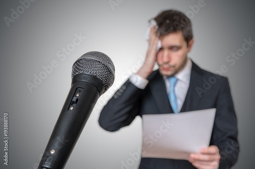 Nervous man is afraid of public speech and sweating. Microphone in front.