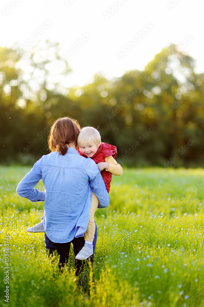 Fototapeta premium Young mother holding her little son during walk in the flowers field