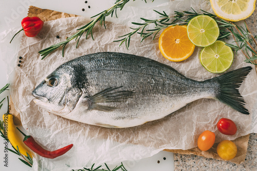 Photography Sea gilt-head bream fish on baking sheet with rosemary, lemon, orange, tomato, hot peppers and lime