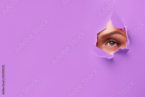 close-up of a female eye that is seen through a hole in bright purple paper © Anna