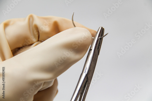 Holding a surgery needle (straight 1/2 circle) with needle holder and hand gloves.