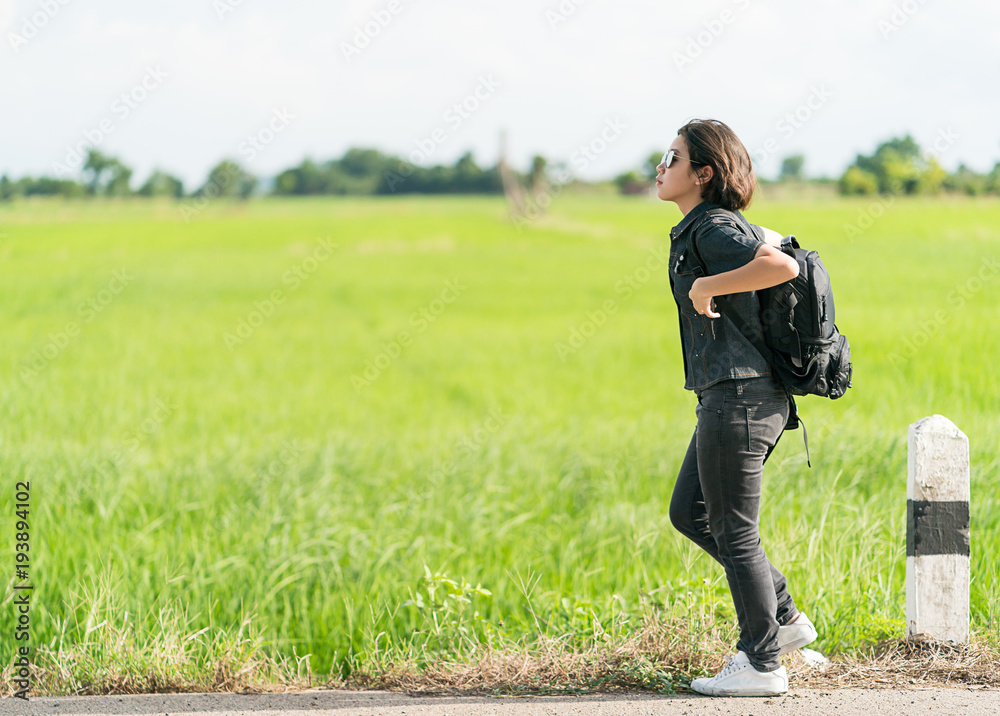 Woman with backpack hitchhiking along a road Woman with backpack hitchhiking along a road
