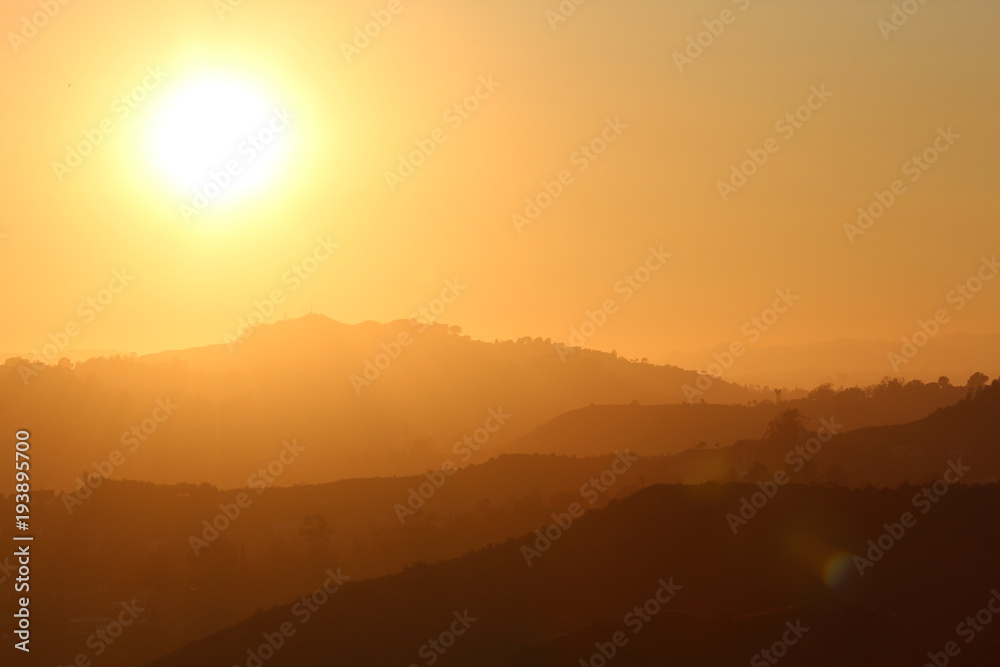 bright yellow sun by a silhouette of layers of mountains