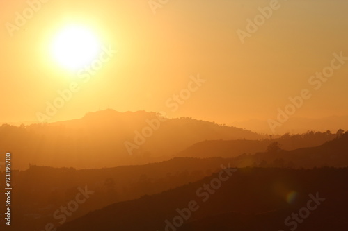 bright yellow sun by a silhouette of layers of mountains