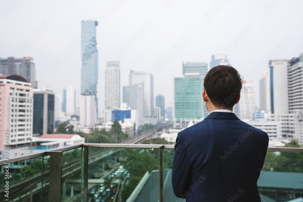 Young businessman standing on balcony looking at city view in Bangkok city, Thailand Young businessman standing on balcony looking at city view in Bangkok city, Thailand