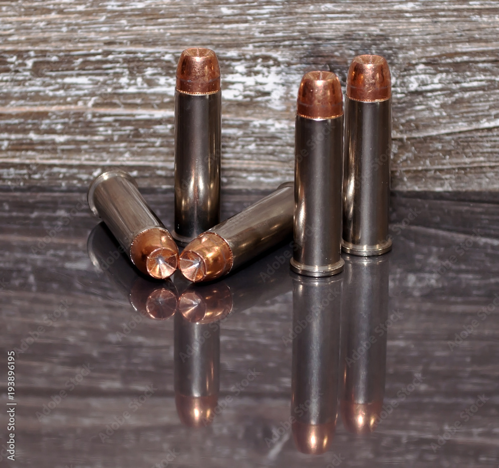 Five .357 magnum bullets with a wooden background and on a reflective surface showing the bullets.