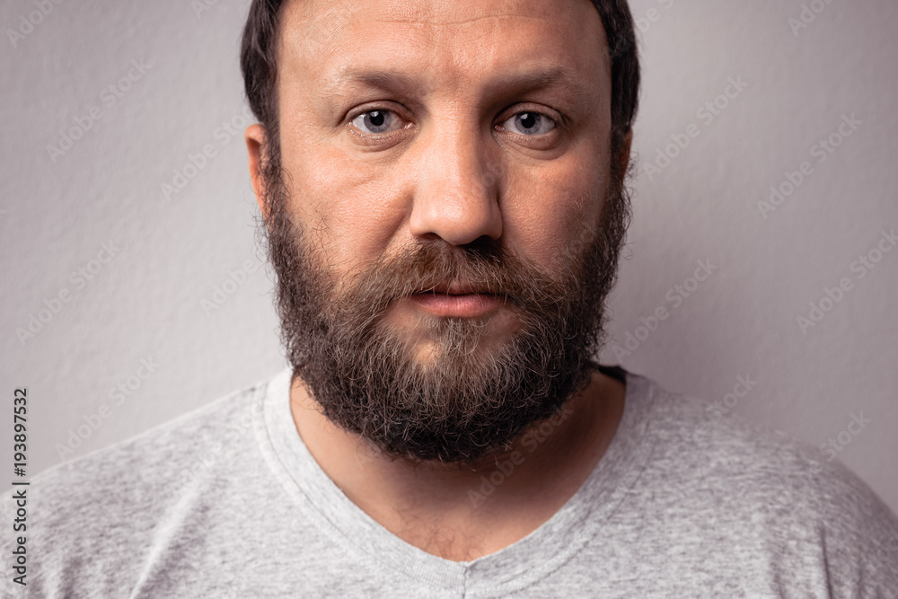 Obraz premium Long beard and mustache of handsome bearded man, portrait of bearded man in gray t-shirt against gray wall.