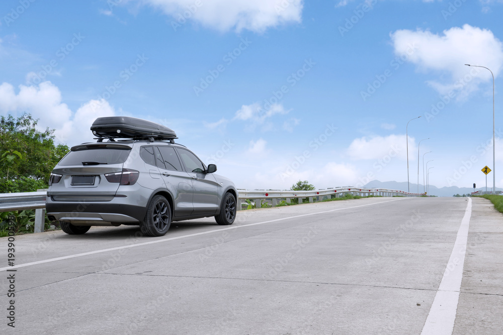 Traveling SUV car with roof box on highway against blue sky