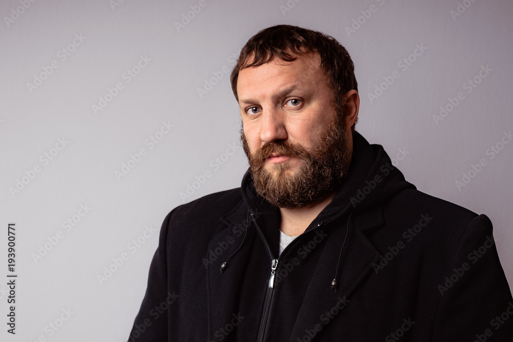 Fashion portrait handsome elegant bearded man wearing black coat against gray background wall.