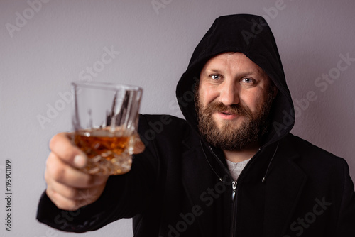 Handsome elegant bearded man wearing black coat with hood drink some strong liquor and smoking his cigar at celebration. © Vlajko611