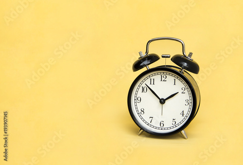 Alarm Clock analog classic vintage retro style black on pale yellow background and copy space.