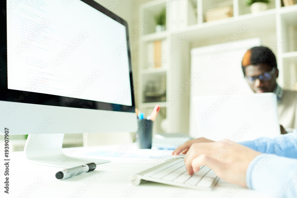 Fototapeta premium Close-up shot of unrecognizable manager sitting at desk and using computer with blank screen, interior of spacious open plan office on background