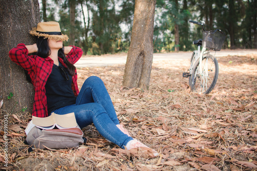 Happy moment hipster woman relaxing and sitting under the big tree on park ,enjoying time on holiday concept ,color of vintage tone and soft focus