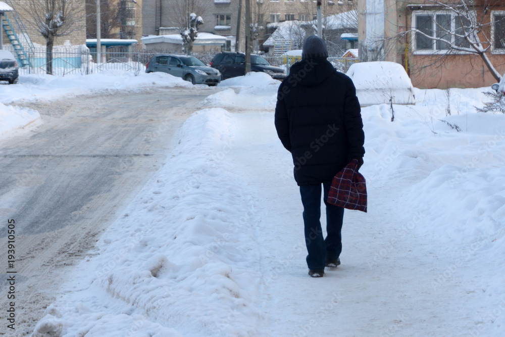 young man in full winter clothes walking outside with shoulder bag .