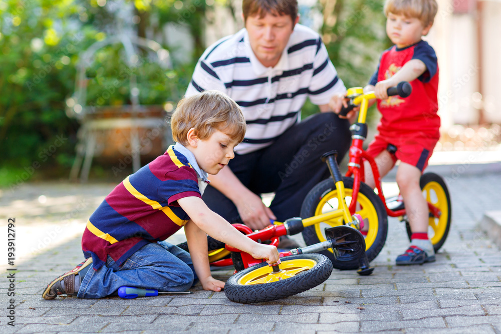 Two happy little kid boys and father repair chain on bikes and change wheel of balance bicycle Two happy little kid boys and father repair chain on bikes and change wheel of balance bicycle