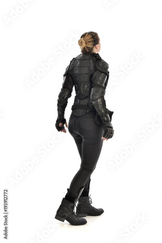 full length portrait of female soldier wearing black tactical armour facing away from camera, isolated on white studio background.