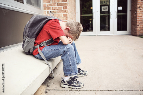 Depressed student sitting outside of school hiding his face