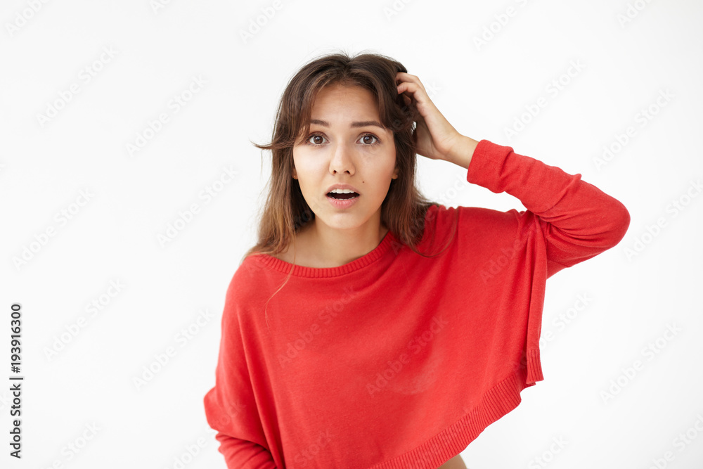 Horizontal shot of stupefied dark haired attractive young mixed race woman staring at camera with shock and astonishment while gossiping with her friends, opening mouth widely and scratching head Horizontal shot of stupefied dark haired attractive young mixed race woman staring at camera with shock and astonishment while gossiping with her friends, opening mouth widely and scratching head