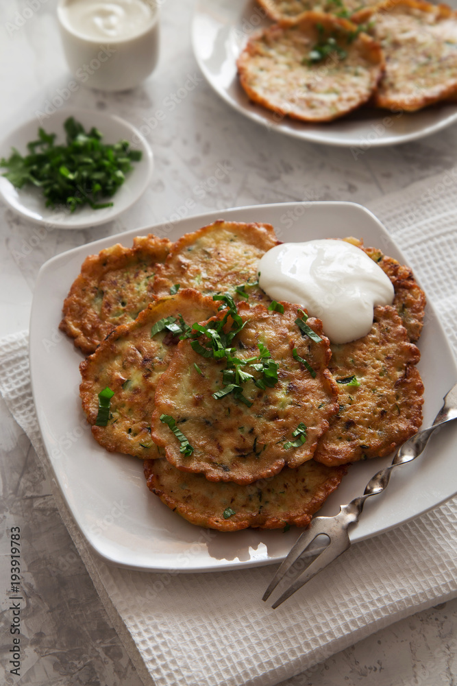 Vegetable pancakes with sour cream on a white plate Vegetable pancakes with sour cream on a white plate