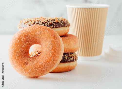 Paper cup of coffee with tasty donuts on white background.