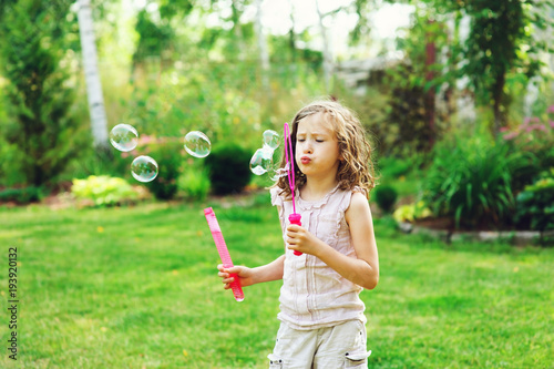 happy kid girl playing with soap bubbles in summer garden