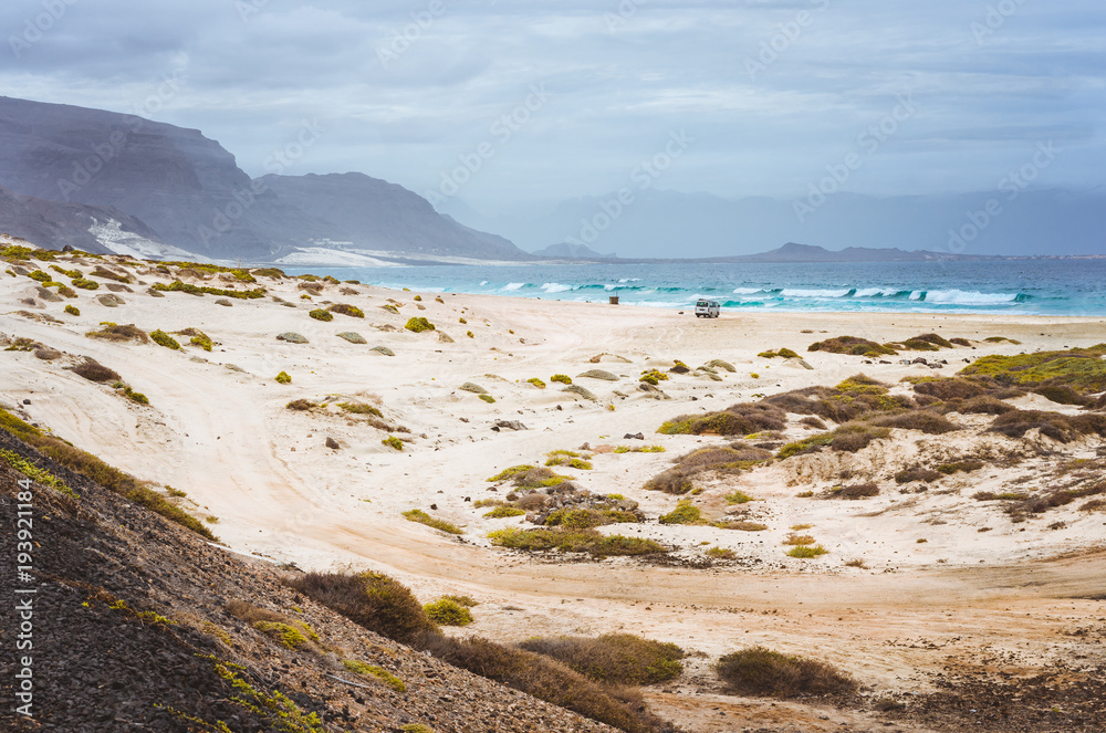 Deserted beach of Praia Grande. Spectacular sand dunes, ocean waves and black volcanic mountains behind. North of Calhau, Sao Vicente Island Cape Verde