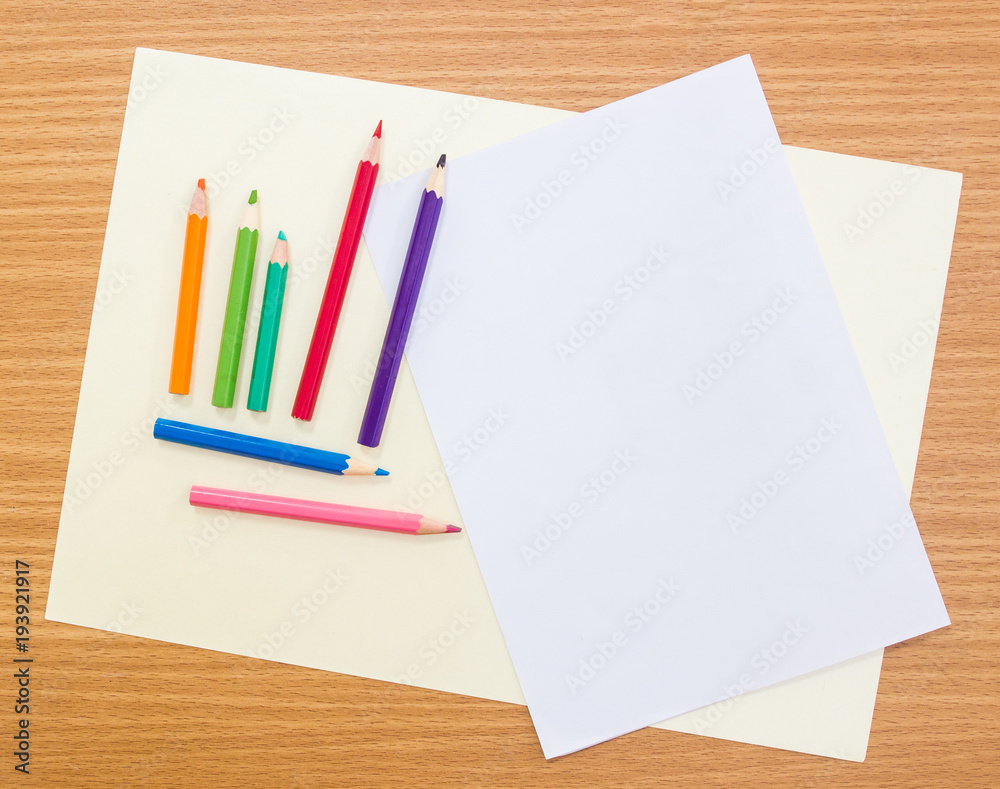 Multicolored crayon pencils lay on grainy white drawing paper over wooden board,top view shot. Multicolored crayon pencils lay on grainy white drawing paper over wooden board,top view shot.