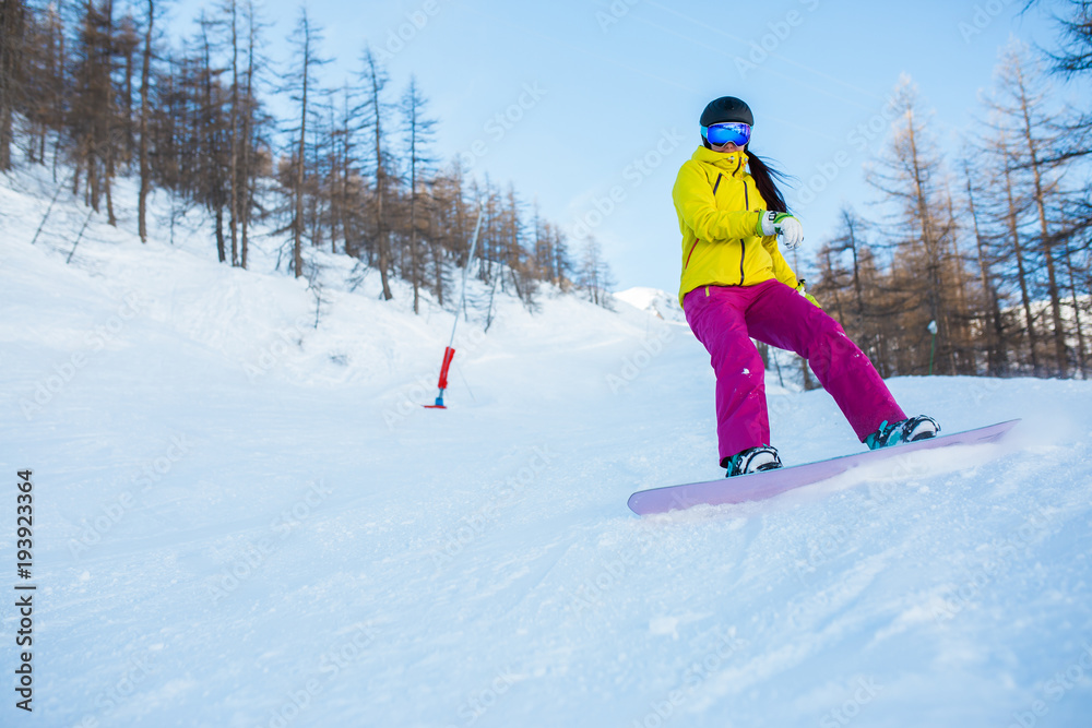 Image of female athlete wearing helmet and mask snowboarding from snowy slope with trees