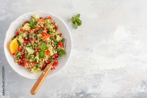 Tabbouleh salad with tomato, cucumber, couscous, mint and pomegranate. Top view, copy space, gray background. Vegan Healthy Food Concept. Traditional middle eastern or arab dish.
