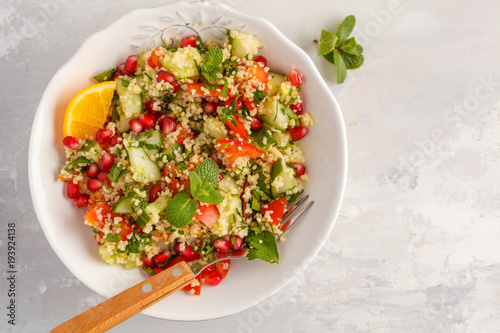 Tabbouleh salad with tomato, cucumber, couscous, mint and pomegranate. Top view, copy space, gray background. Vegan Healthy Food Concept. Traditional middle eastern or arab dish.