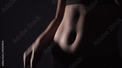 Slim young woman drinking water after training a on a black background. belly sports girl close-up photo