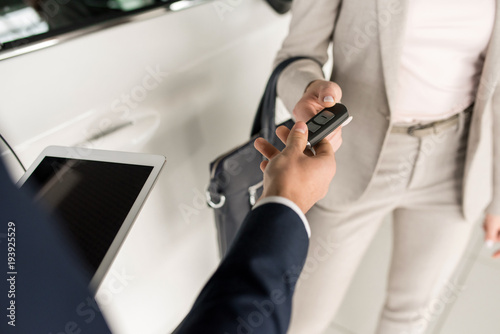 High angle close up of car salesman giving keys to client standing next to white luxury car, copy space © Seventyfour