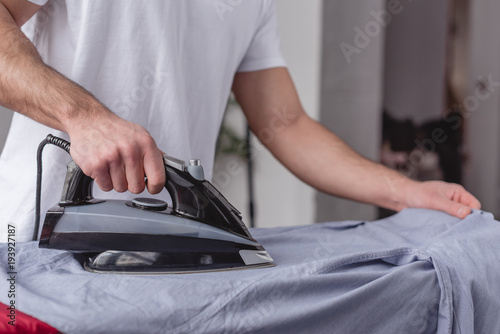 cropped image of man ironing shirt on ironing board in living room